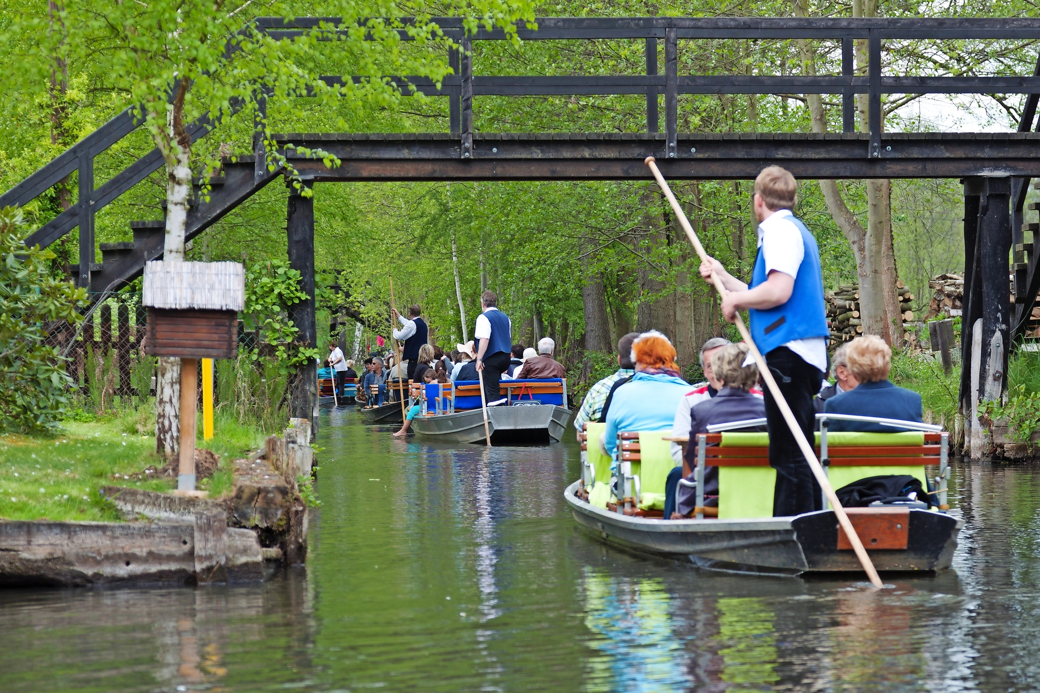 Personen auf Kähnen fahren durch einen grünen, von Bäumen umgebenen Kanal.