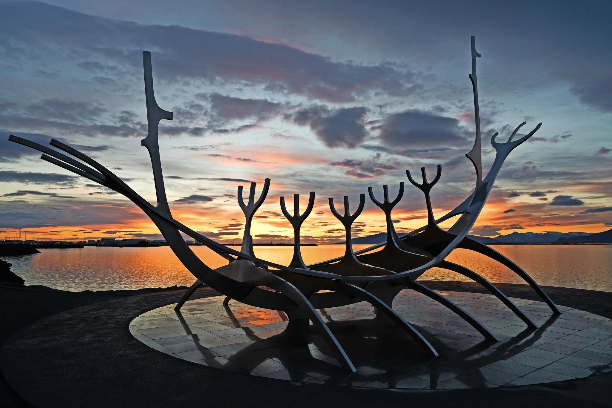 Skulptur eines Wikingerschiffs vor einem farbenfrohen Sonnenuntergang am Wasser.