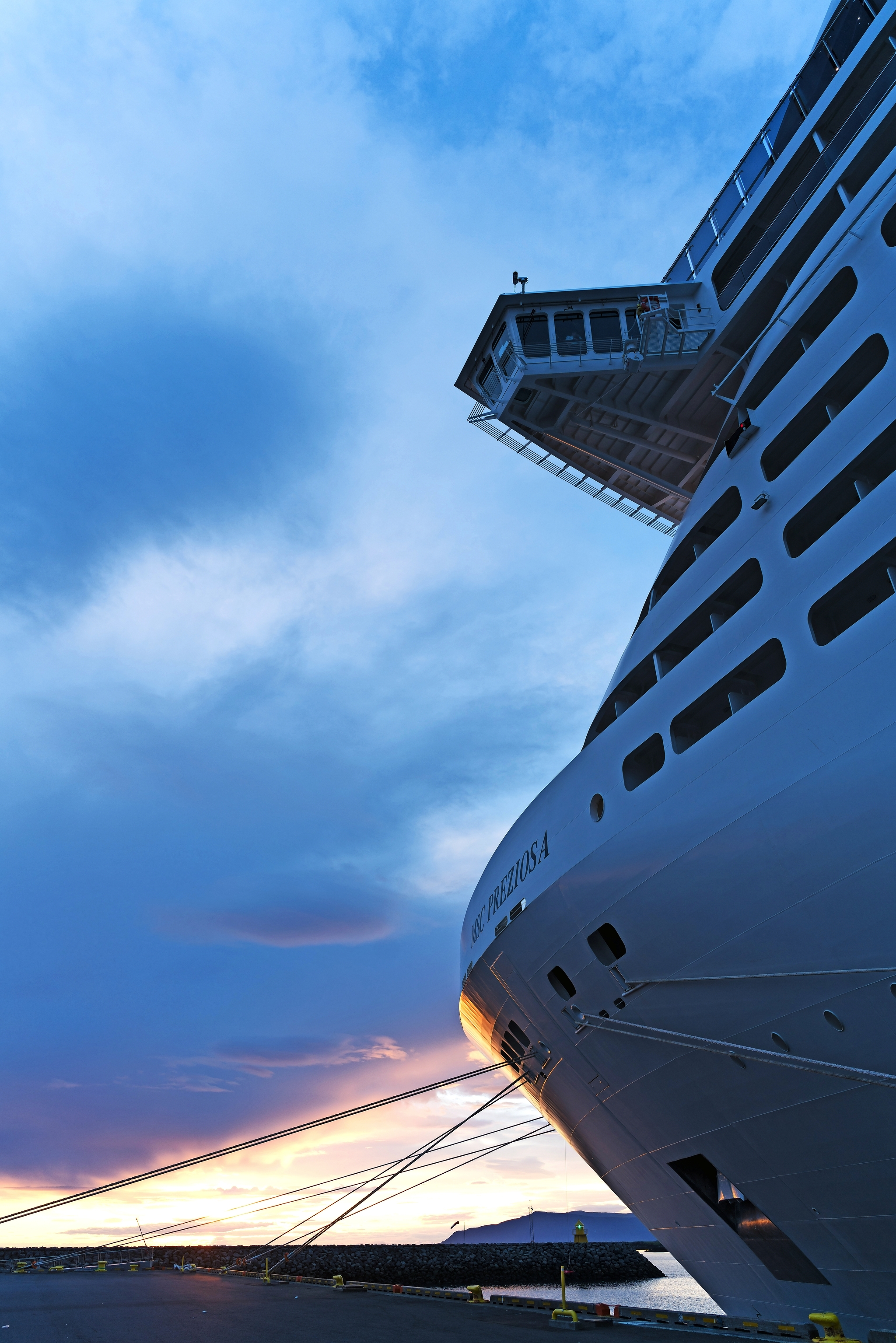 Großes Kreuzfahrtschiff im Hafen bei Sonnenaufgang mit dramatischem Himmel im Hintergrund.