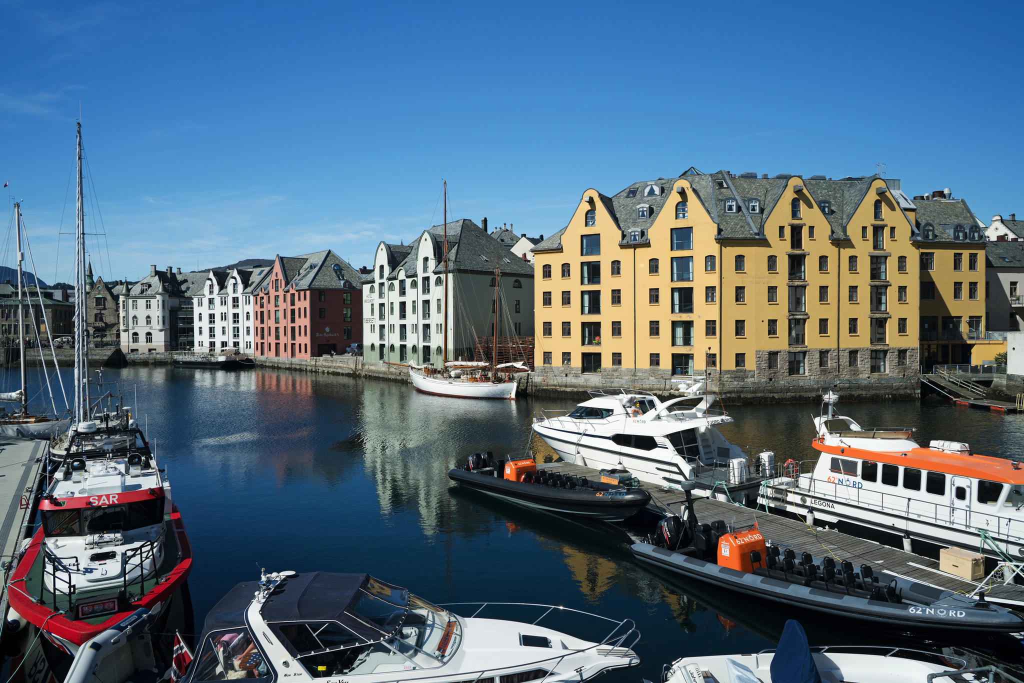 Bunte Häuser am Wasser mit Booten in einem norwegischen Hafen bei klarem Himmel.