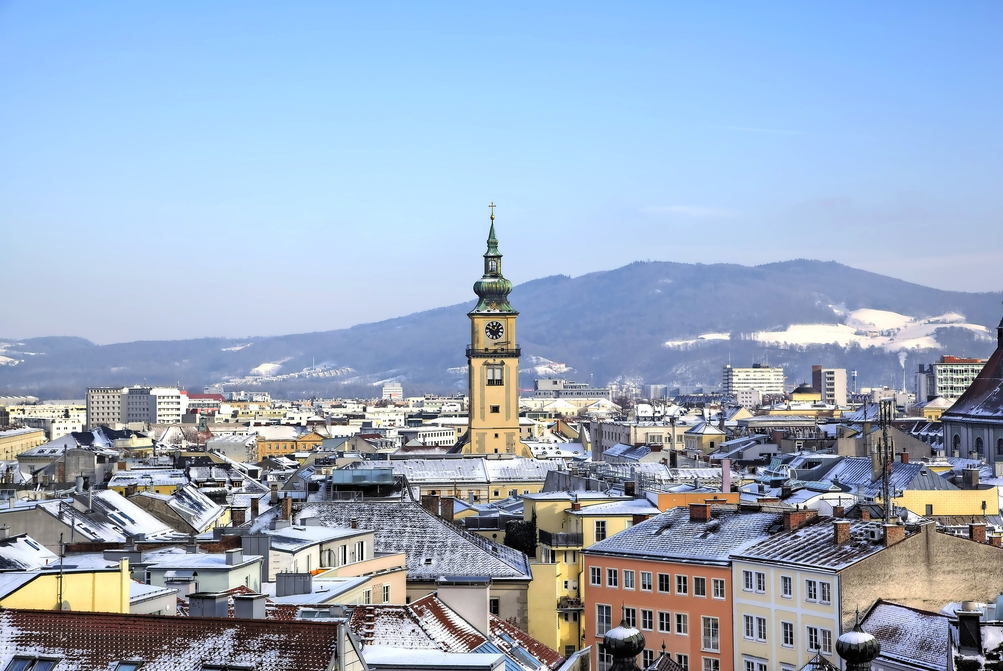 Stadtpanorama mit Kirchturm vor schneebedecktem Berg im Hintergrund.