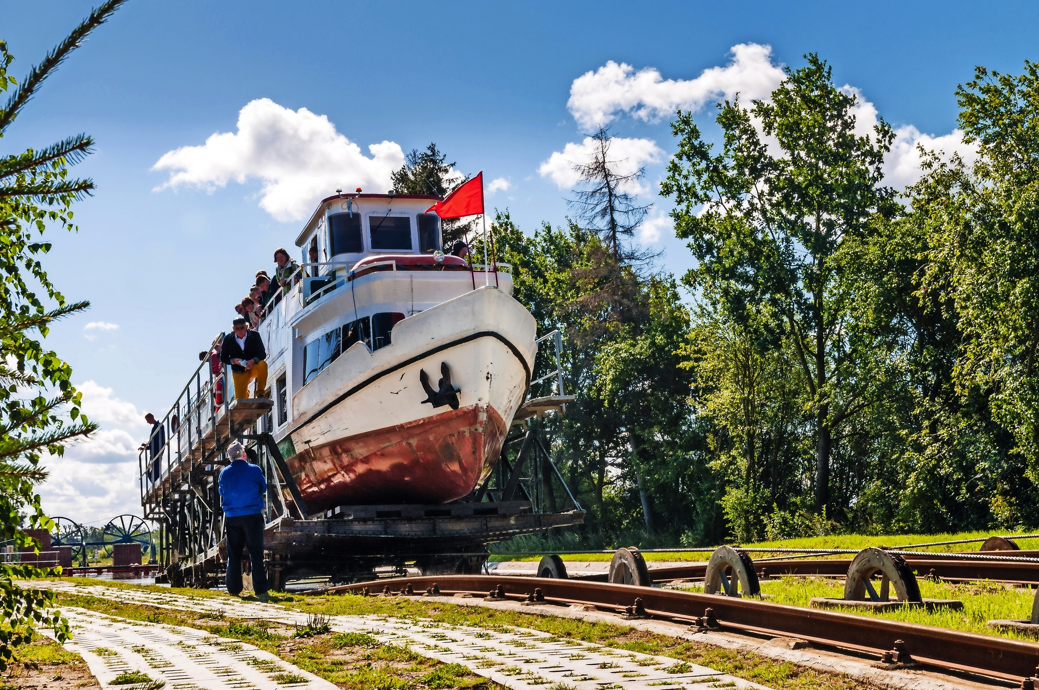 Ein Boot wird auf einer Schienenrampe transportiert, umgeben von Bäumen und blauem Himmel.