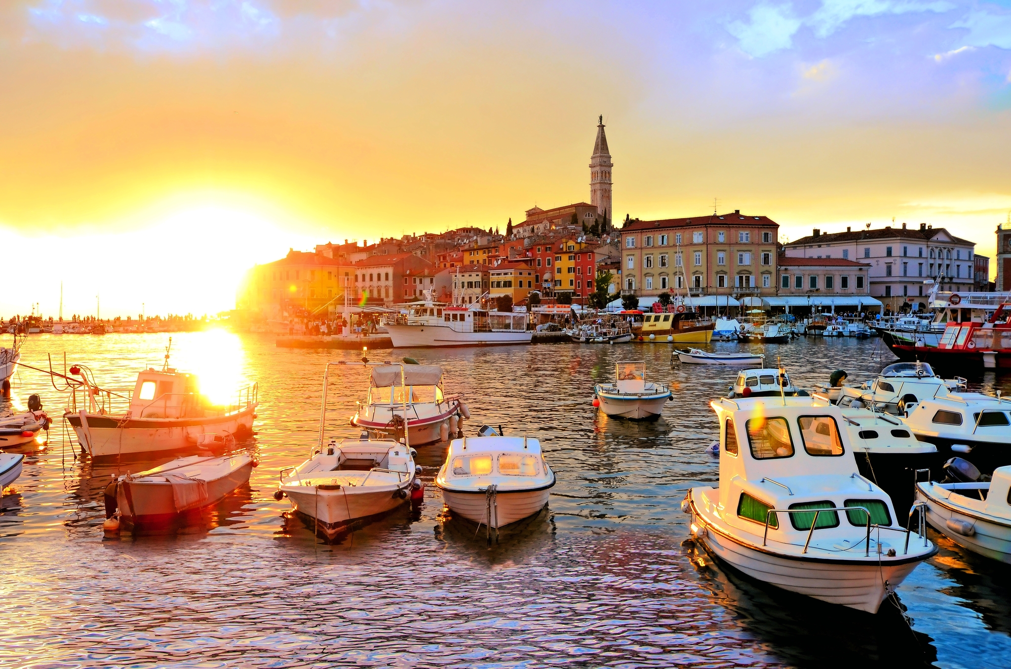 Boote in einem Hafen bei Sonnenuntergang mit einer Altstadt im Hintergrund.