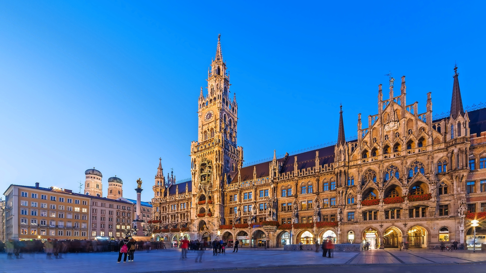 Neues Rathaus in München bei Abenddämmerung, Menschen auf dem Platz davor.