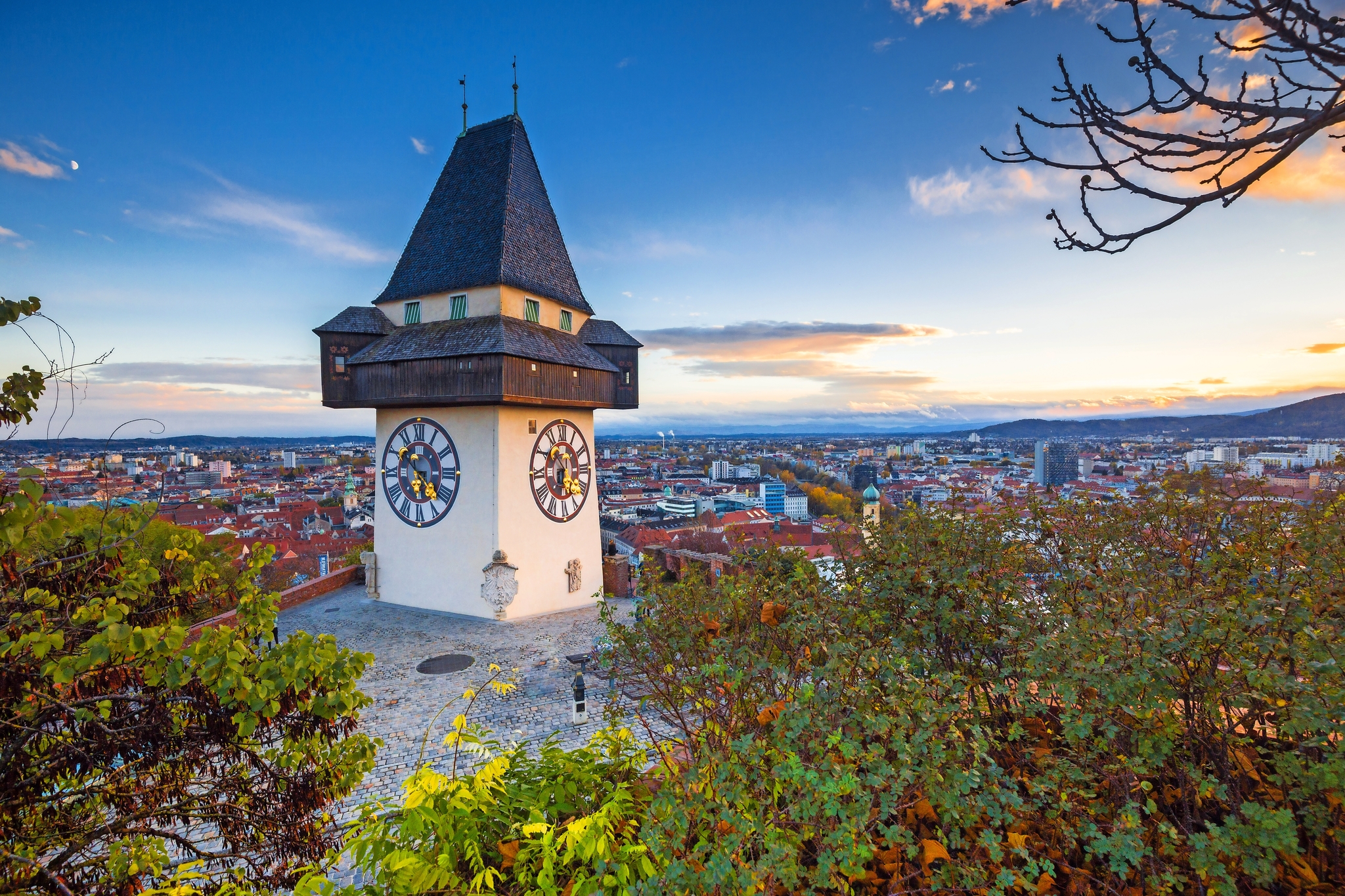 Uhrturm auf Hügel mit Stadt im Hintergrund bei Sonnenuntergang.